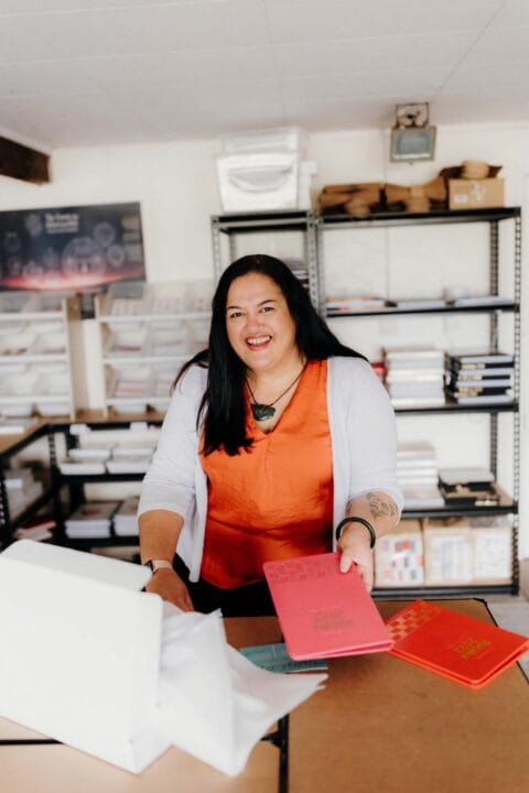 Geneva Harrison holding a Tuhi Stationery planner and wearing an orange top and greenstone necklace