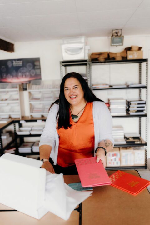 Geneva Harrison holding a Tuhi Stationery planner and wearing an orange top and greenstone necklace