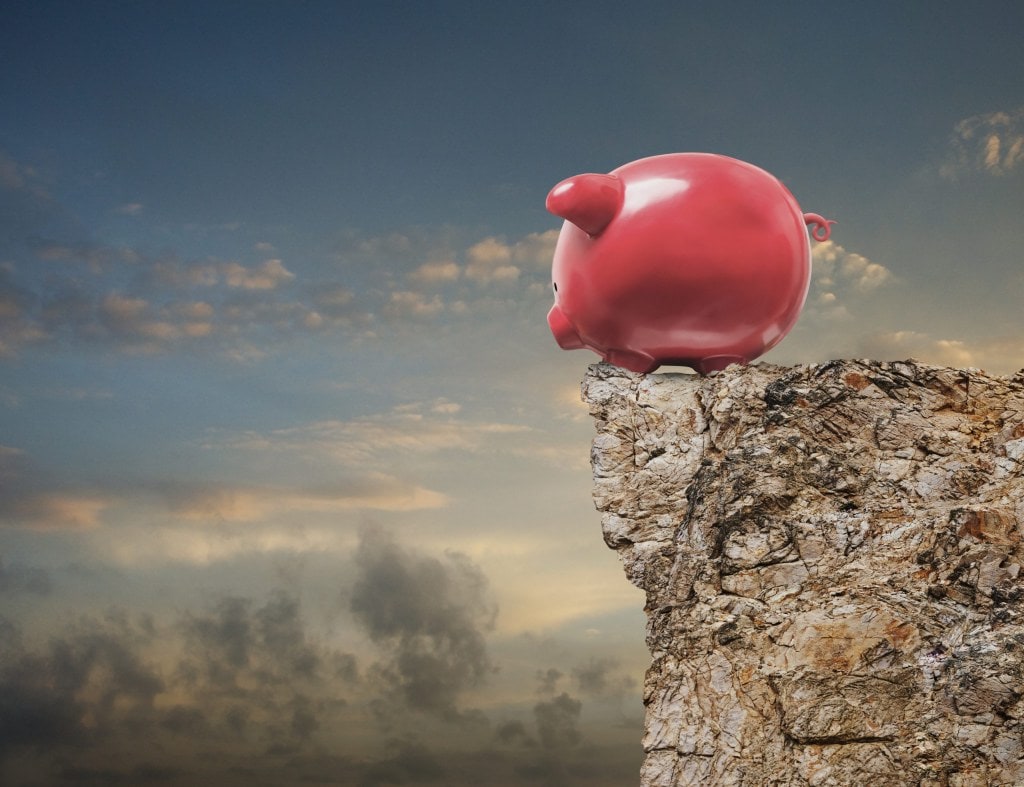 A piggy bank stands at the edge of a cliff and looks over in an image about investment decisions, risk, and challenge.