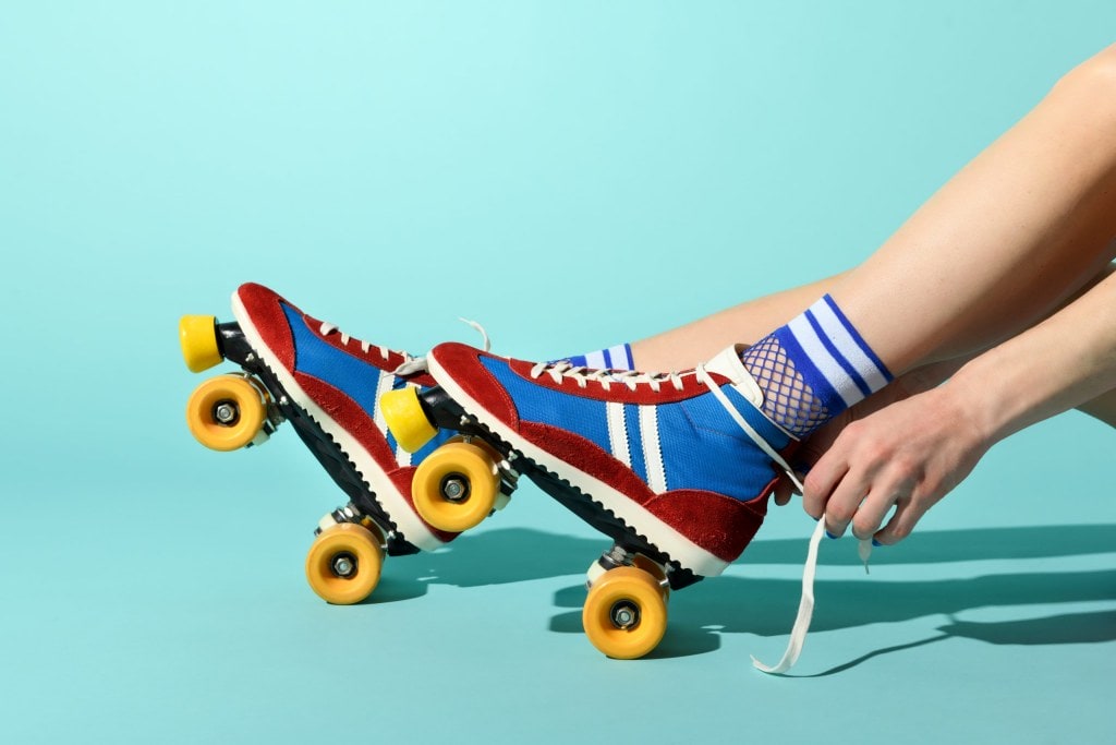 Young woman tying the laces on her red and blue rollerskates with colorful yellow wheels in a close up side view of her feet and hands over a blue background with copyspace
