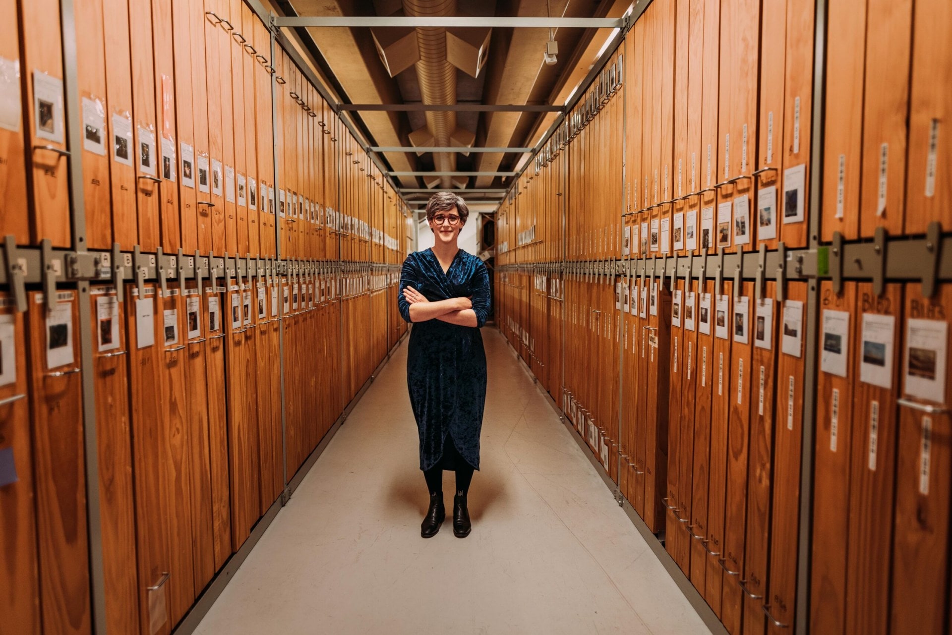 Lizzie Bisley standing with arms crossed in a brown hallway with lockers on either side