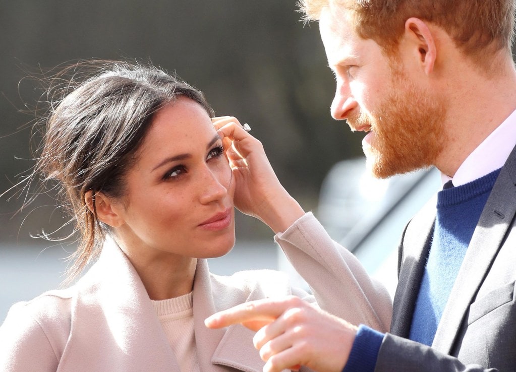 Meghan Markle wearing pink coat looking at Prince Harry while he's speaking