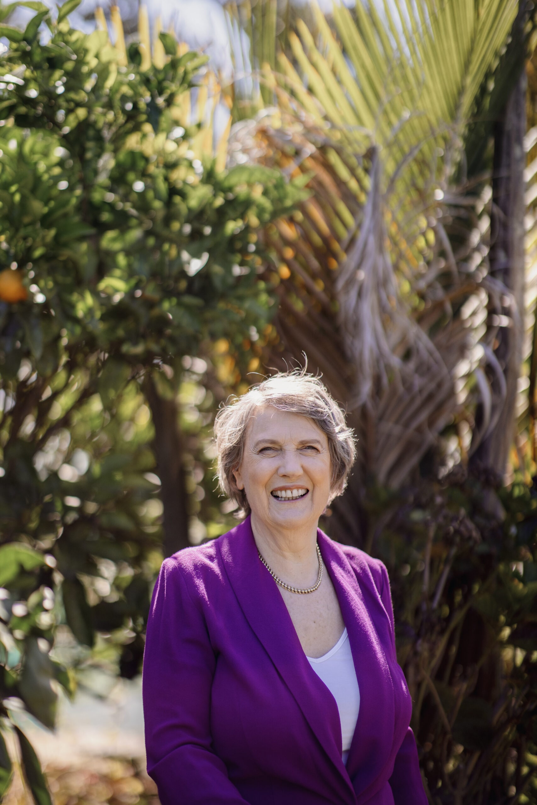 Helen Clark standing in garden wearing purple jacket