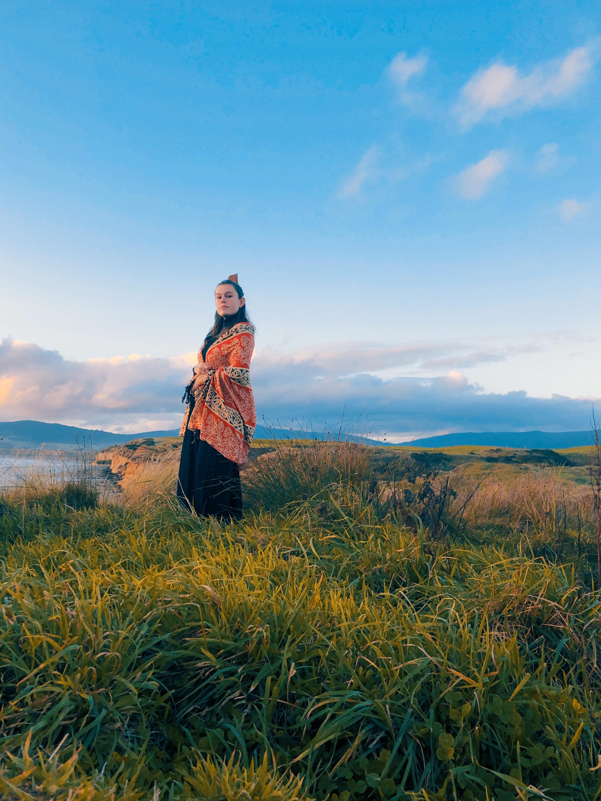 Jess Thompson Carr wearing a traditional Māori cloak standing on top of a hill