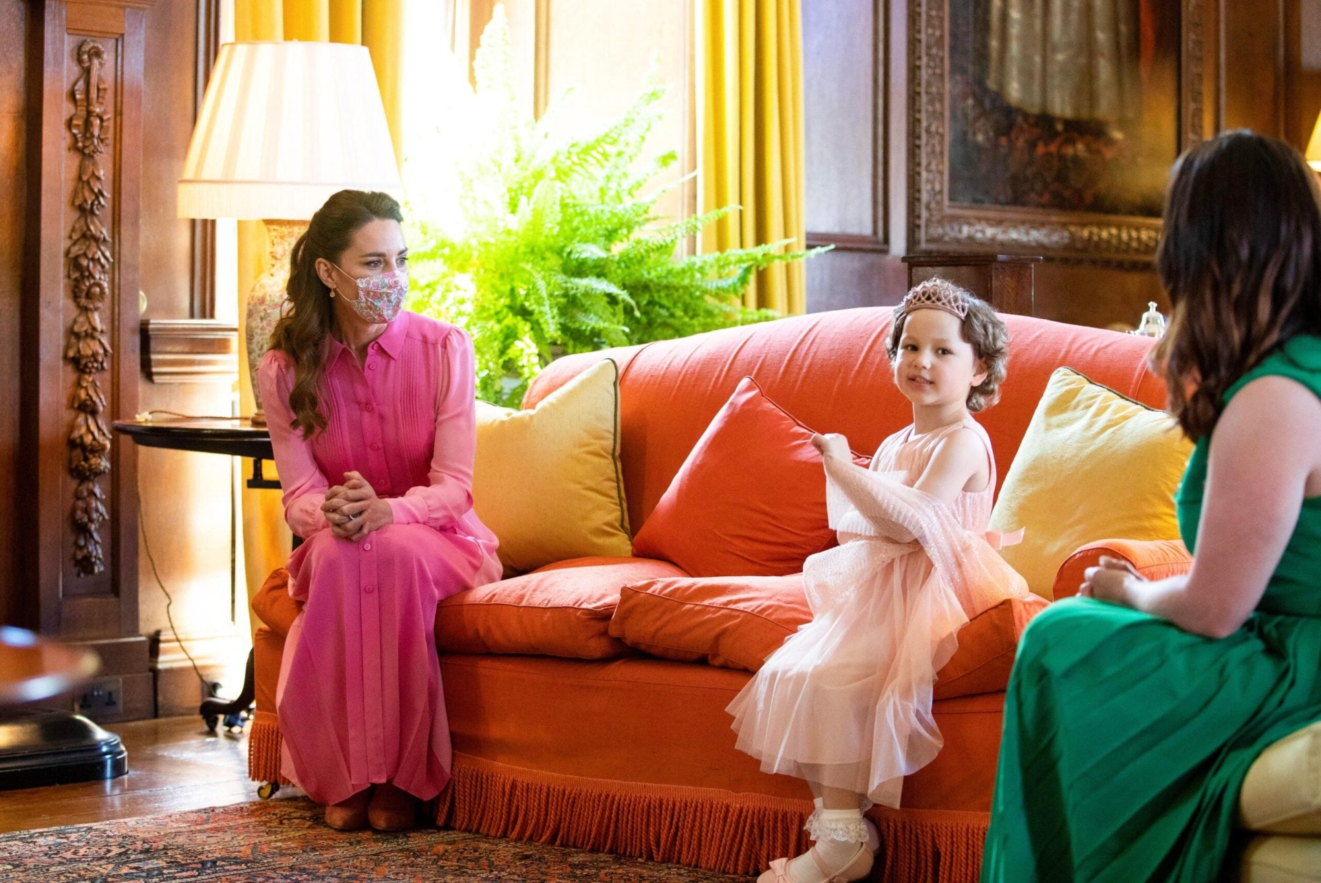 Kate Middleton Duchess of Cambridge sitting on an orange couch with Mila Sneddon