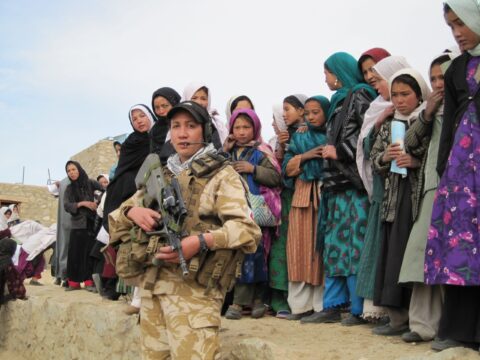 A woman holding a gun standing in front of several children