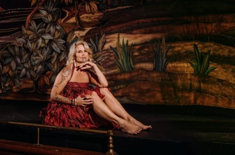 Dr Hinemoa Elder sitting on a stage wearing red dress