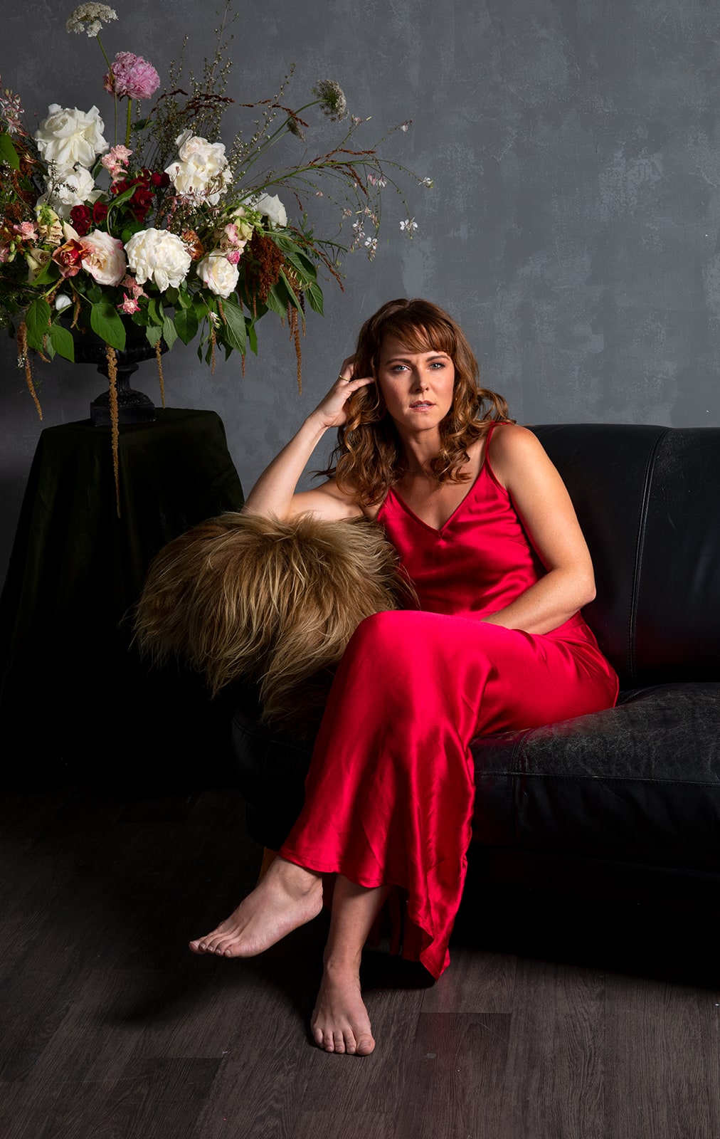 Ria Vandervis sitting on couch wearing red silk dress 