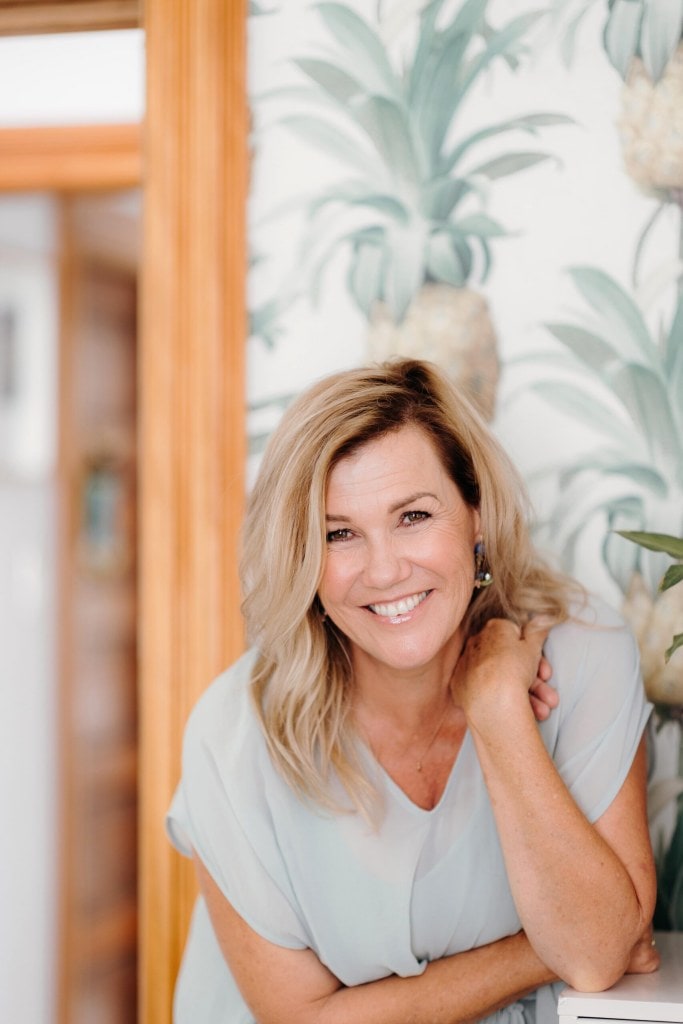 Robyn Malcolm smiling while leaning to the camera and wearing a light blue top