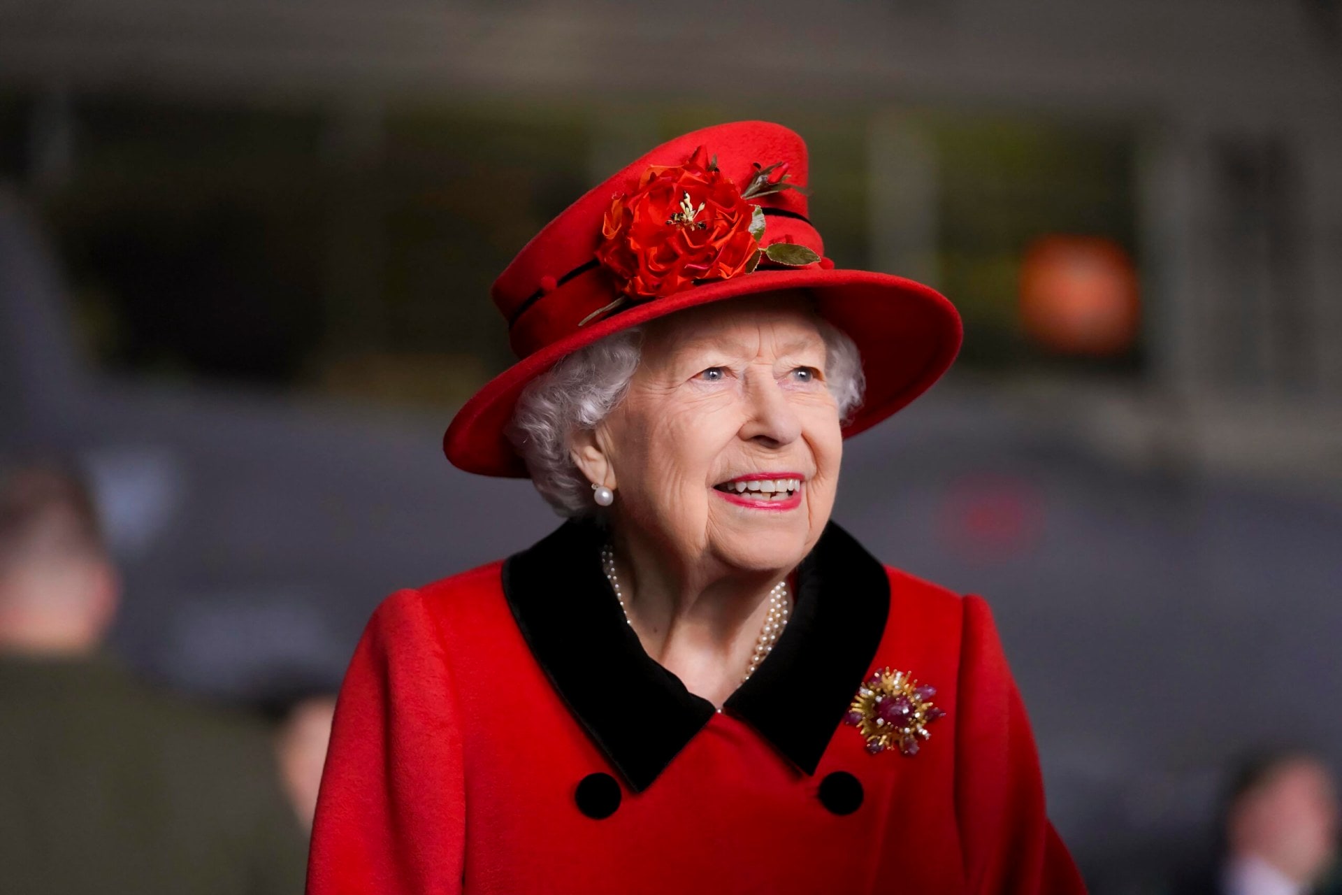 Mid-shot of Queen Elizabeth II wearing a red coat with black trimmings and matching red hat 