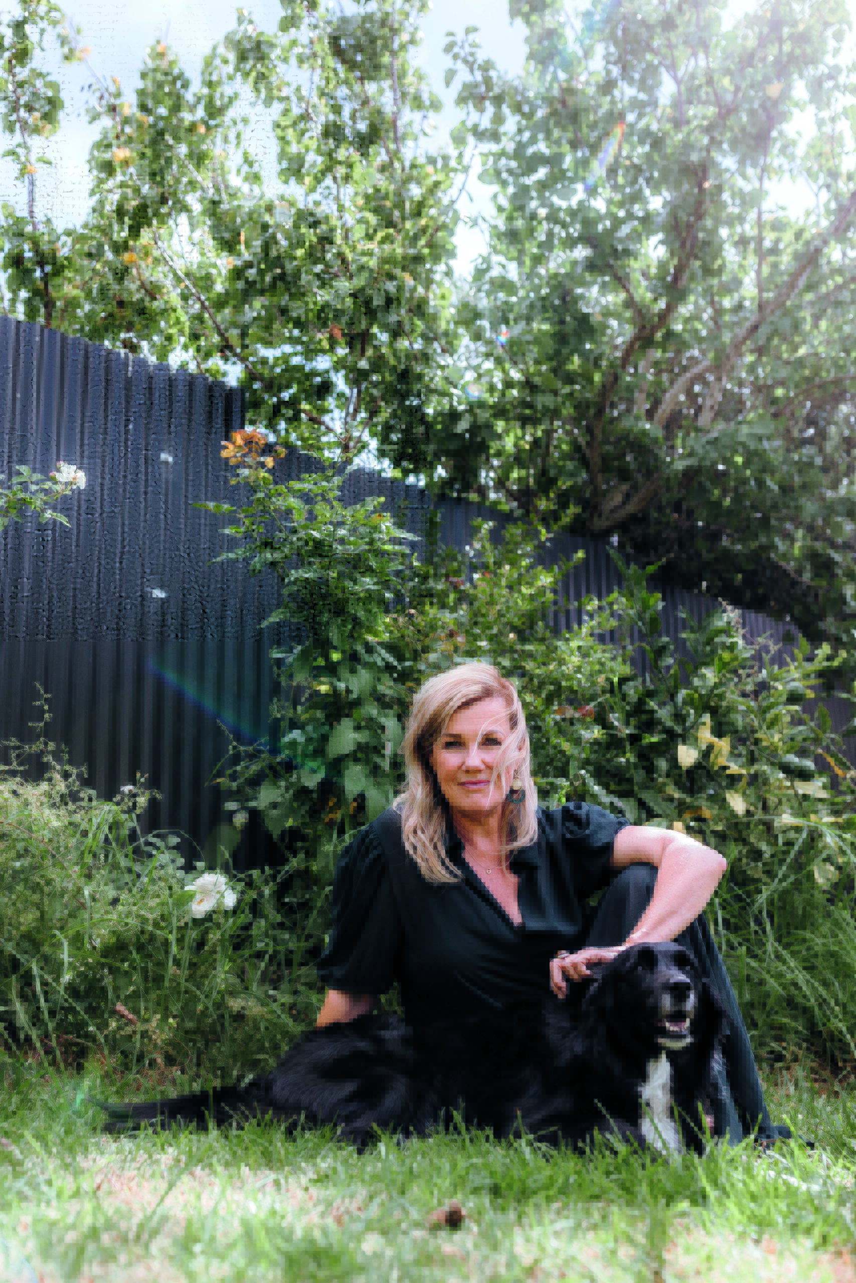 Robyn Malcolm wearing a black dress and sitting in a garden with her pet dog