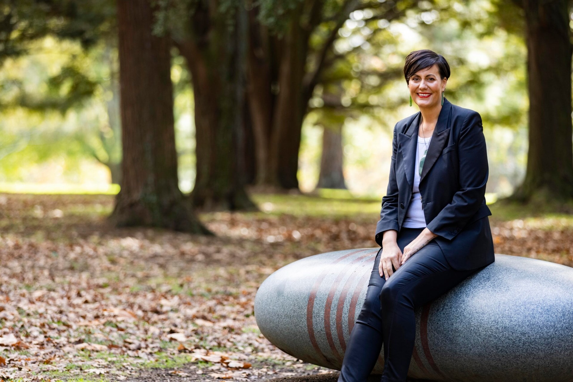 Rachel Taulelei sitting on a large grey rock statue wearing a black blazer, black pants and white top