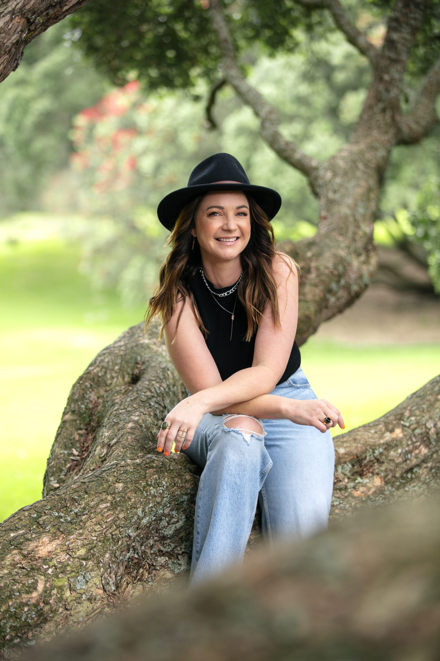 Claire Chitham wearing black hat and top while sitting on tree