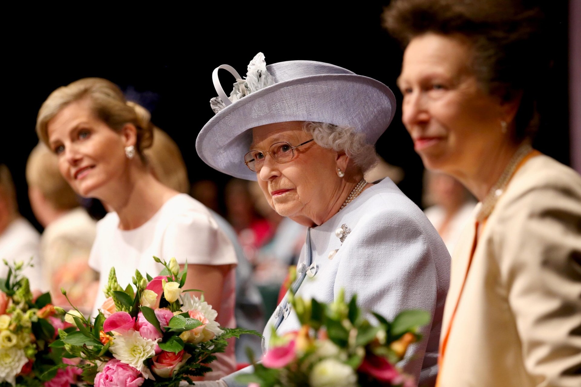 Sophie, Countess of Wessex, Princess Anne, Princess Royal and Queen Elizabeth II sitting at a flower covered table together at Women's Institute Celebrating 100 Years cake at the Centenary Annual Meeting of The National Federation Of Women's Institute at Royal Albert Hall