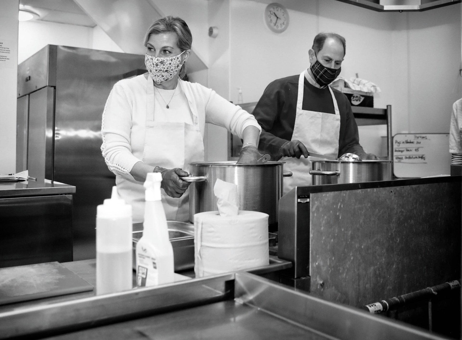 Black and white photo of countess Sophie, Countess of Wessex and Prince Edward cooking in the kitchen of a community centre
