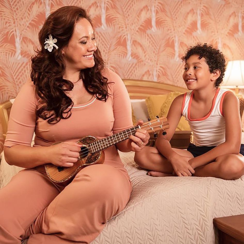 Stacey Leilua playing a ukulele to Adrian Groulx in a scene from Young Rock