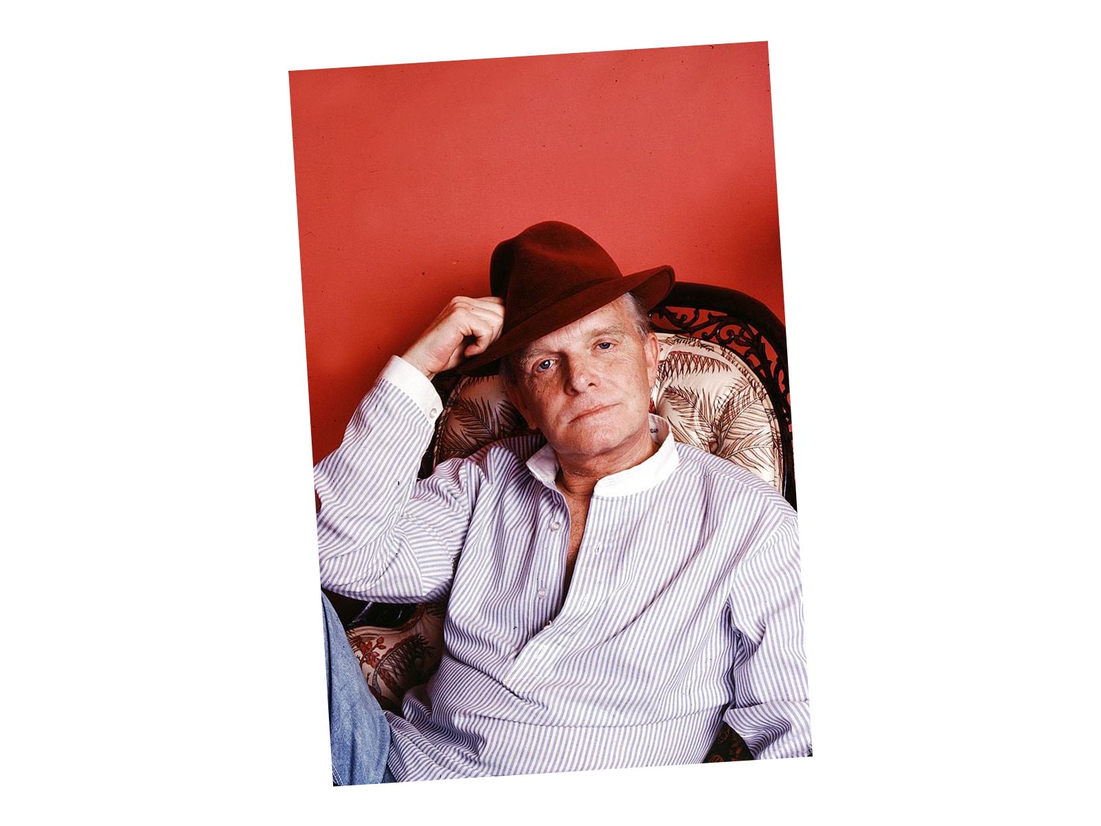 Truman Capote wearing trilby hat and striped blue and white top sitting in a chair