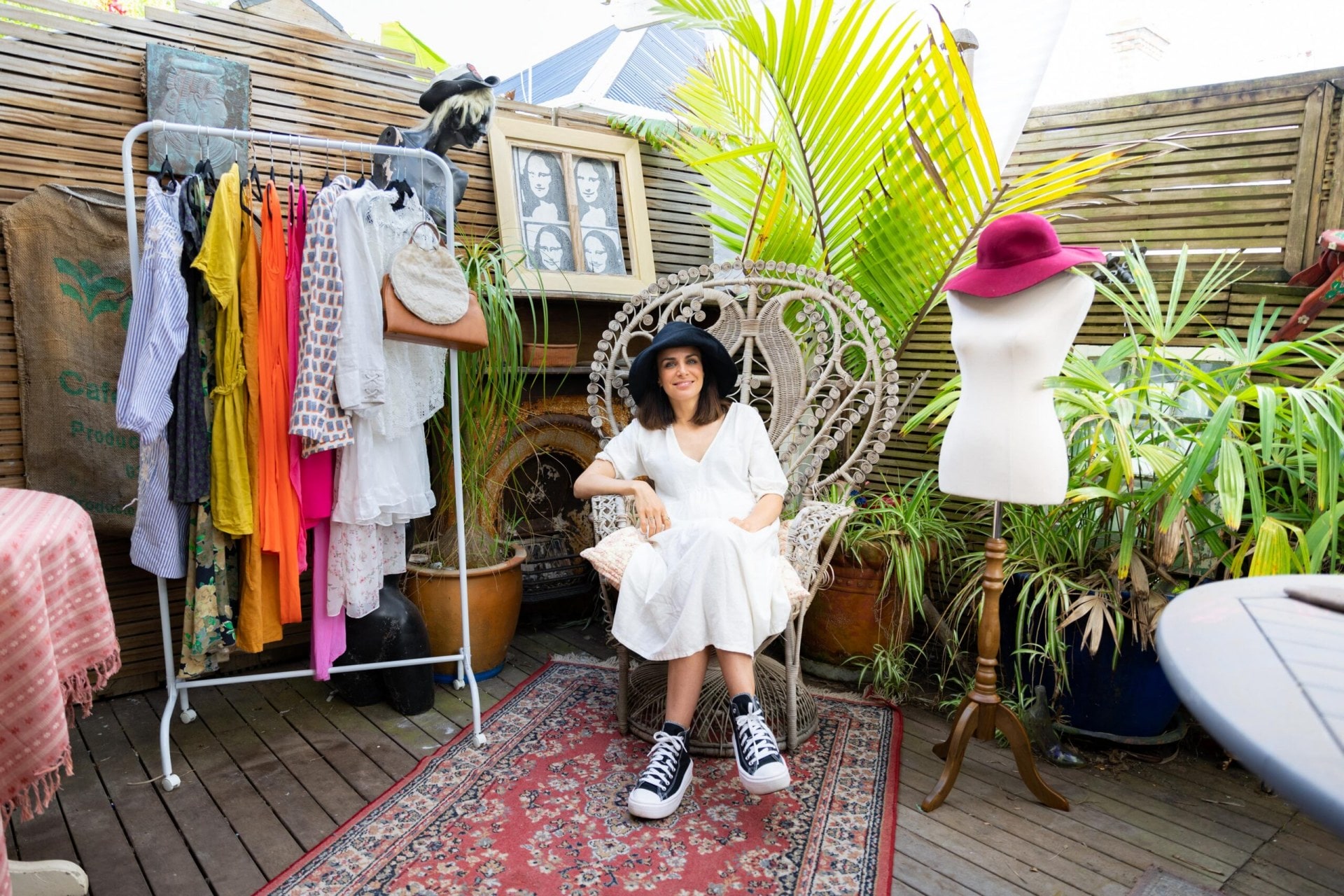 Tab Coleman sitting in a rattan chair outside on a deck with a rug on the deck and a clothes rack next to her