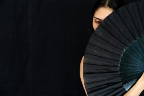 woman holding a black fan in front of her face