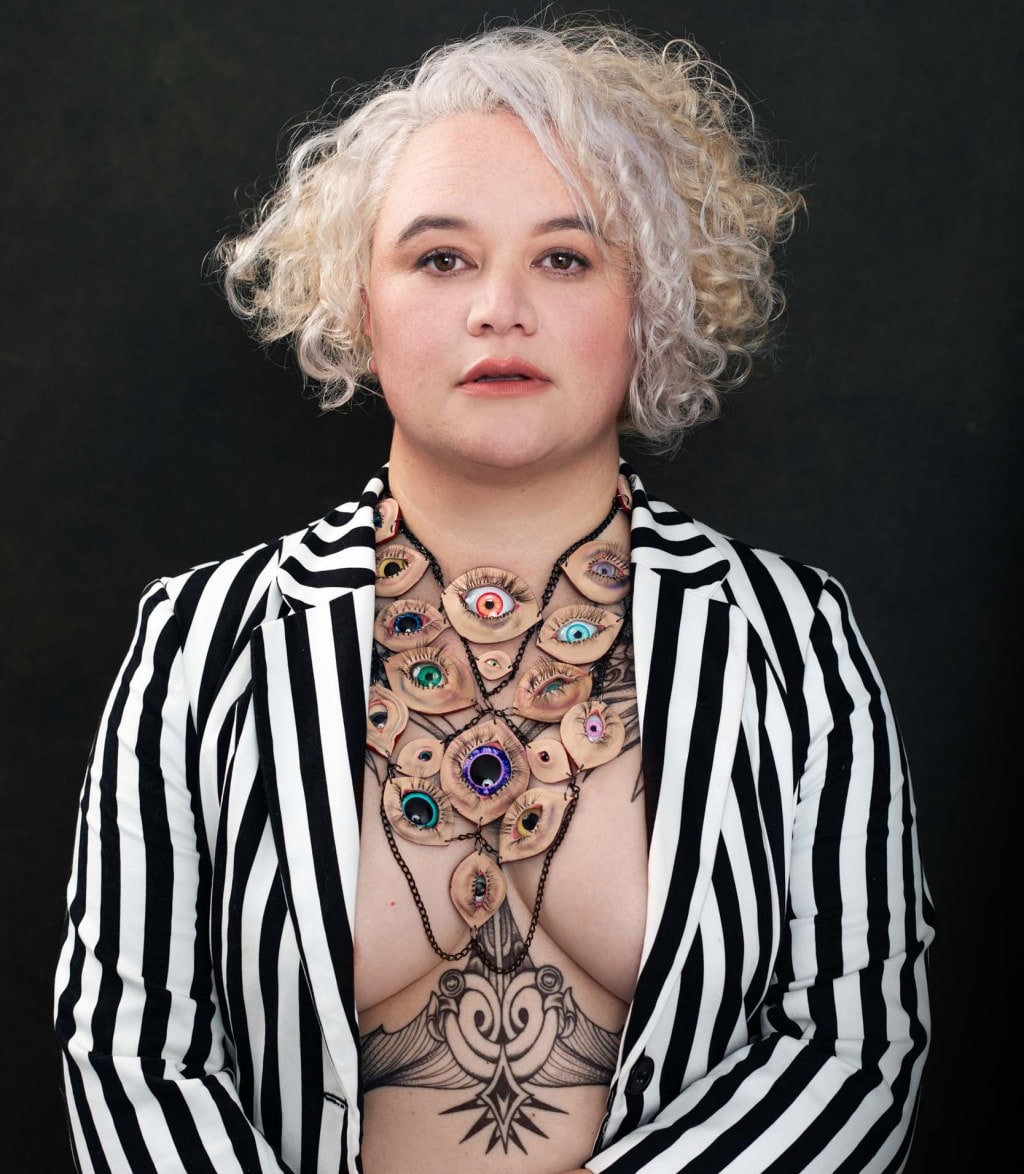 portrait of a woman wearing a black and white striped jacket with tattoos on her chest
