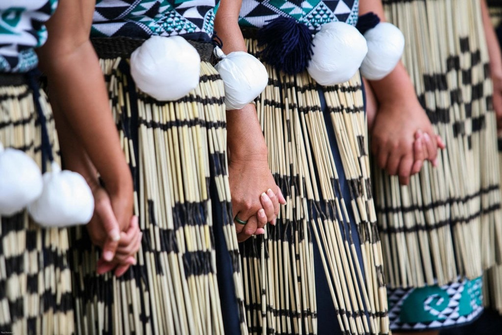 a line of people wearing piupiu and poi holding hands