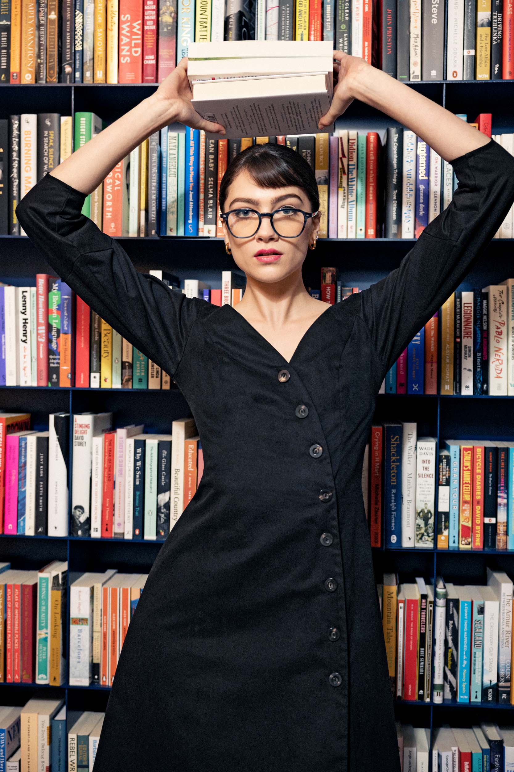 a model in a black dress and glasses standing in a bookstore