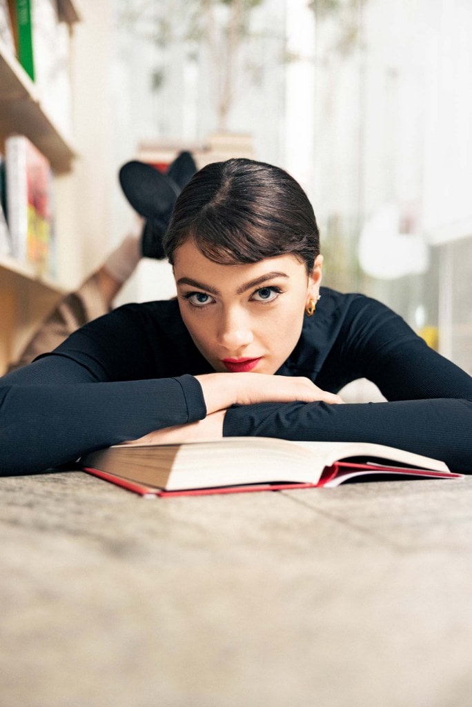 a dark haired model lying down with a book
