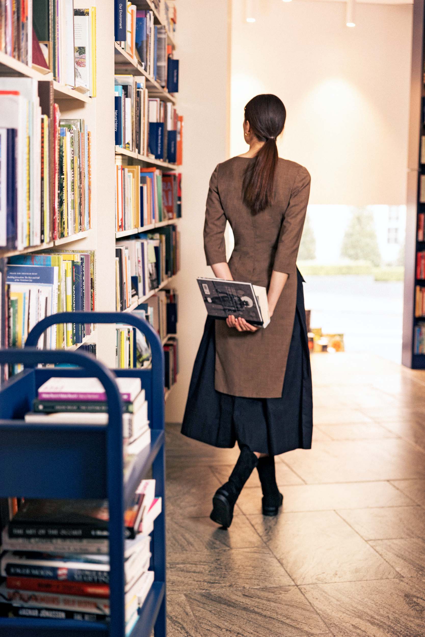 a model wearing a brown jacket holding books behind her back