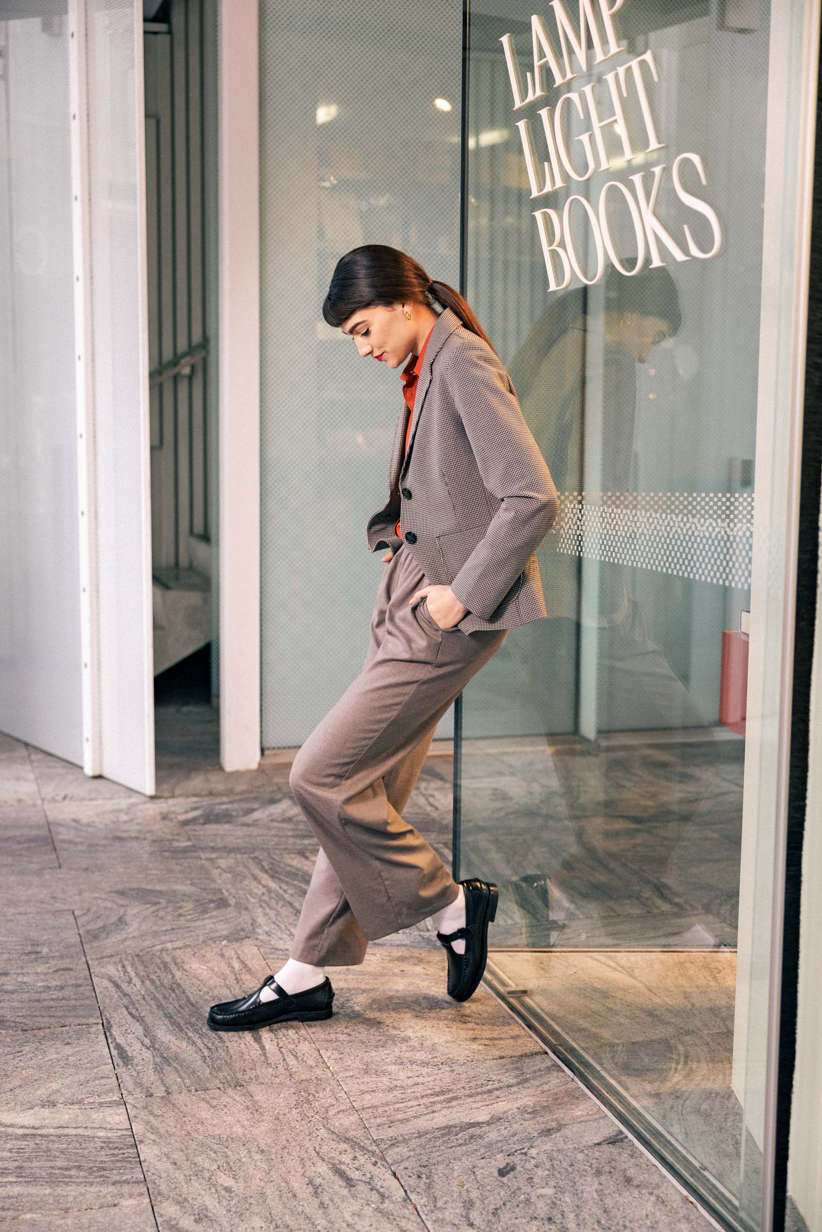 a woman leaning against glass wearing a grey suit