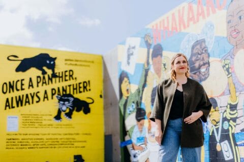 Charlotte Ryan standing in front of a yellow wall that says once a panther always a panther