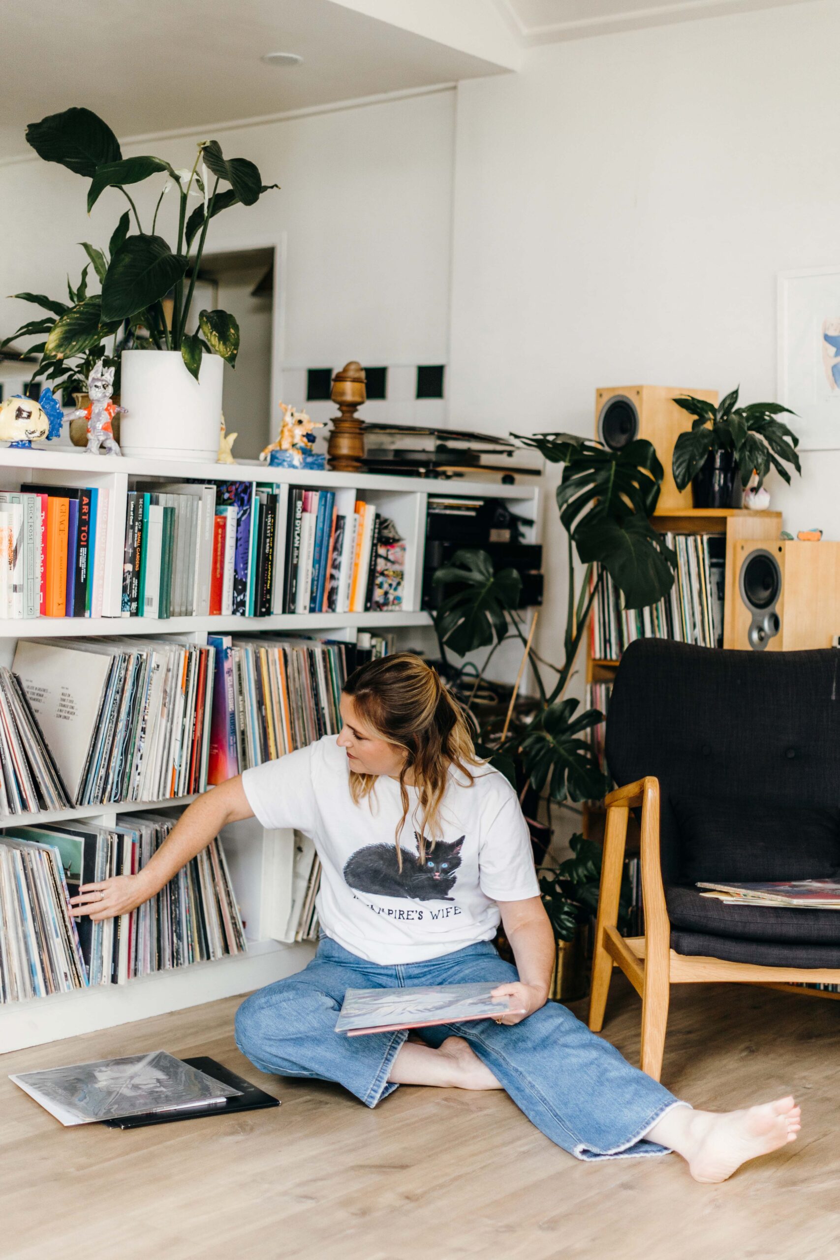 Charlotte Ryan in a t-shirt and jeans sitting on the floor pulling records out of the shelving behind her