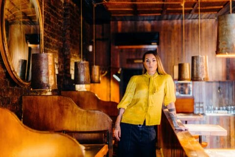 Hollie Smith in a yellow top leaning with one hand on a bar