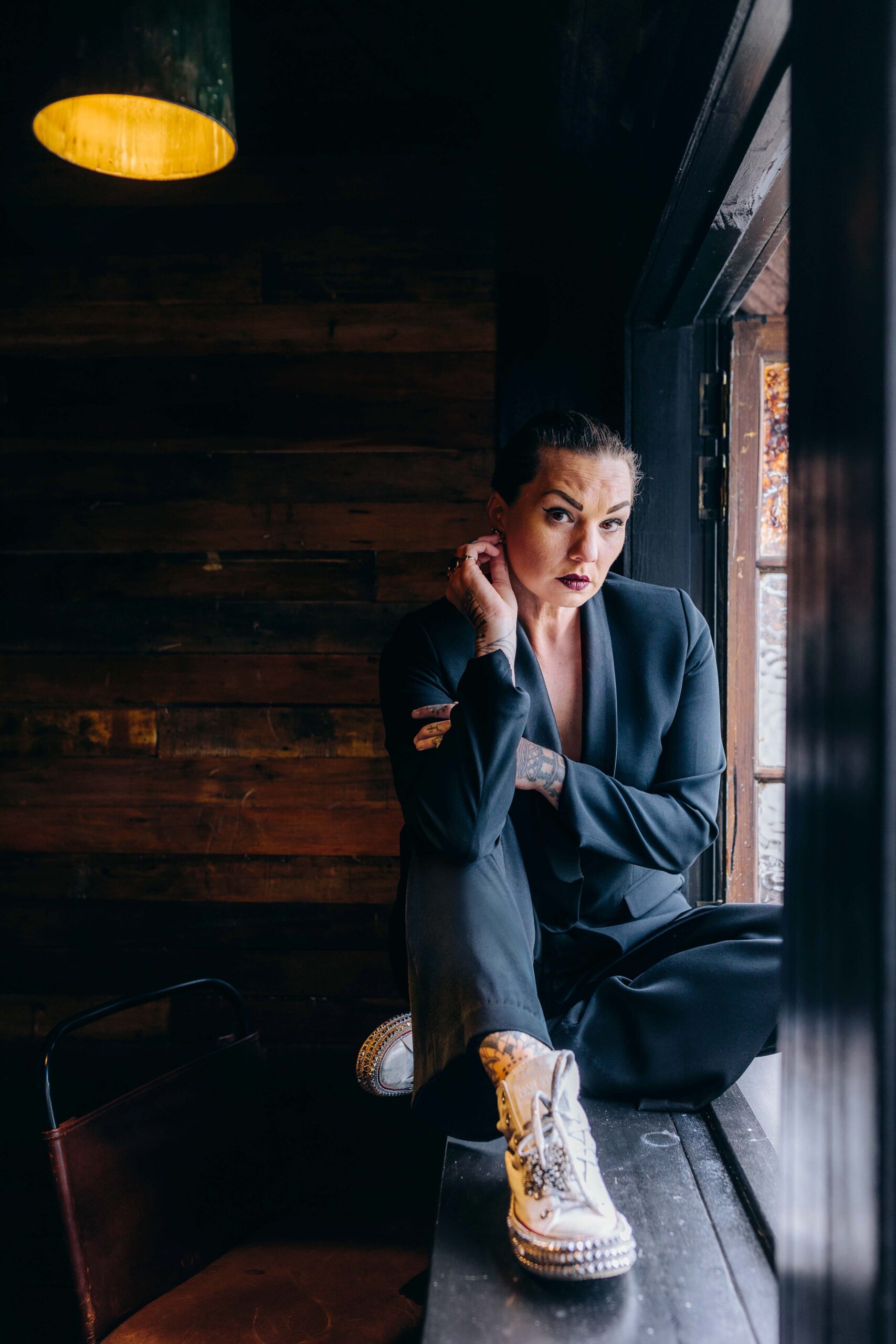 Hollie Smith in a charcoal suit and white converse sitting on a window ledge