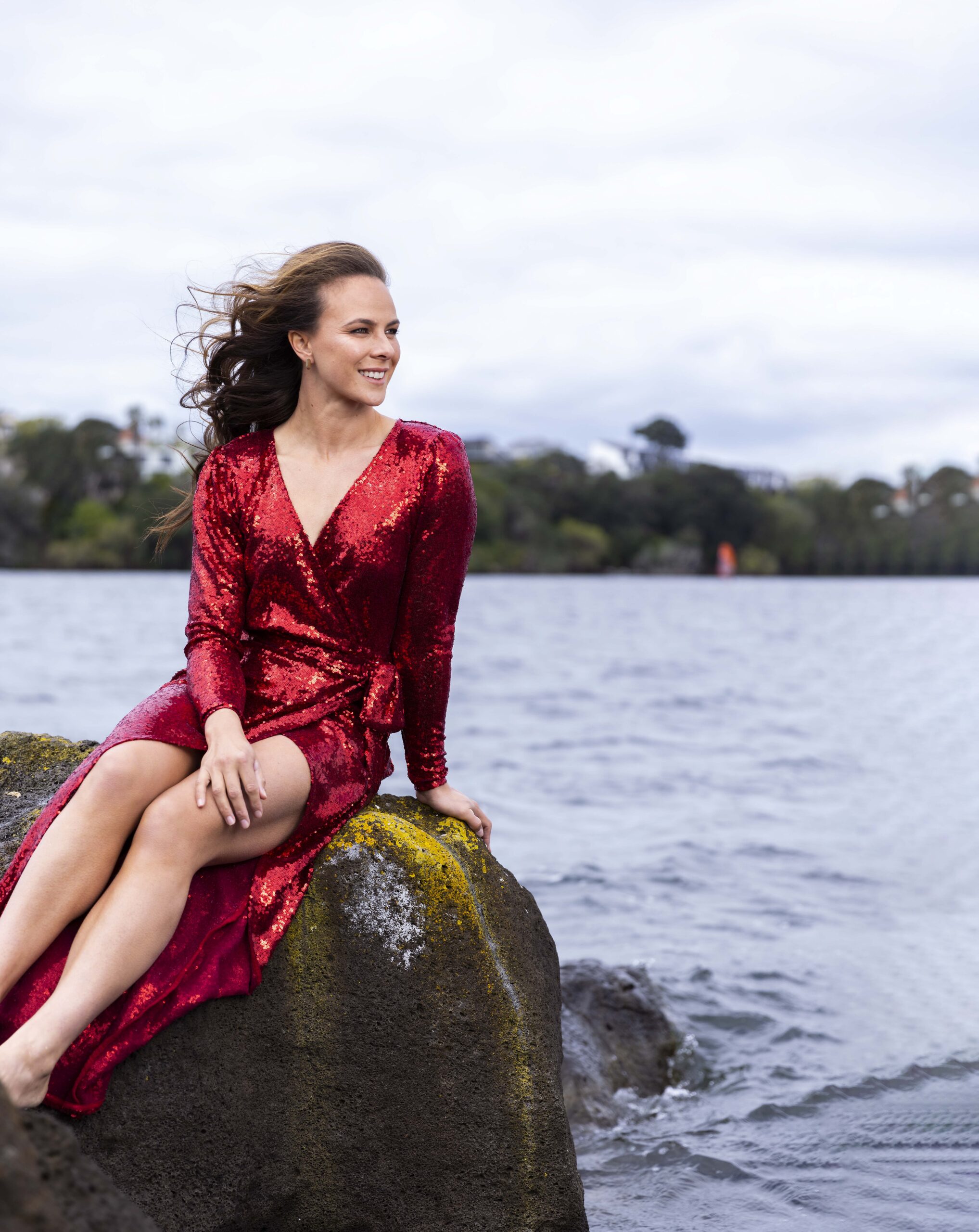 Lisa Carrington in a sparkly red dress sitting on a rock beside a lake