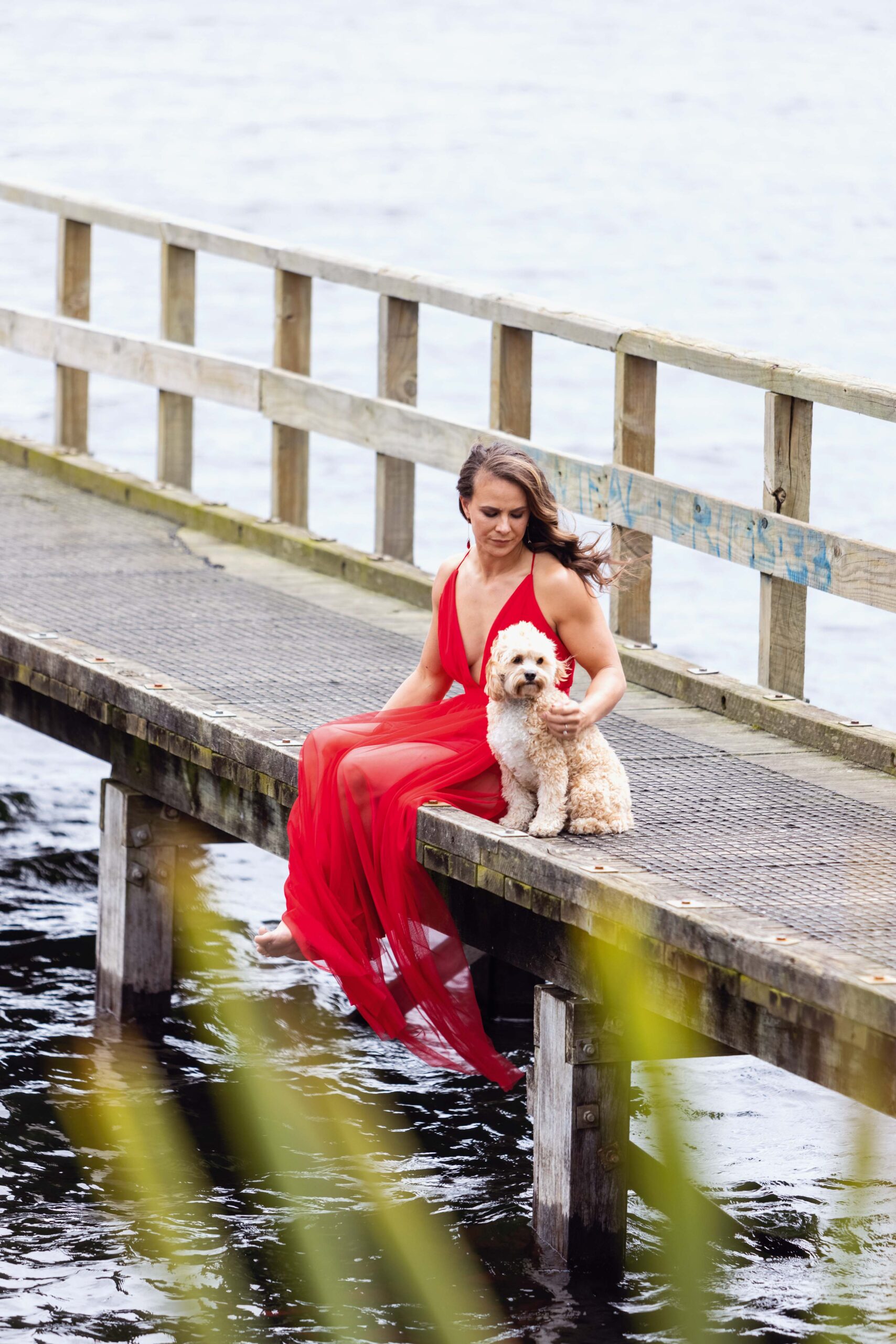Lisa Carrington in a red dress sitting on a pier with her dog