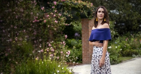 Nadine Higgins in a blue top and floral skirt holding her hand across her waist