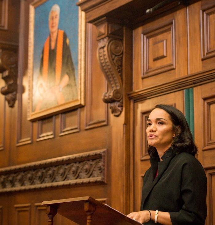 Tiana in black at a wooden lectern