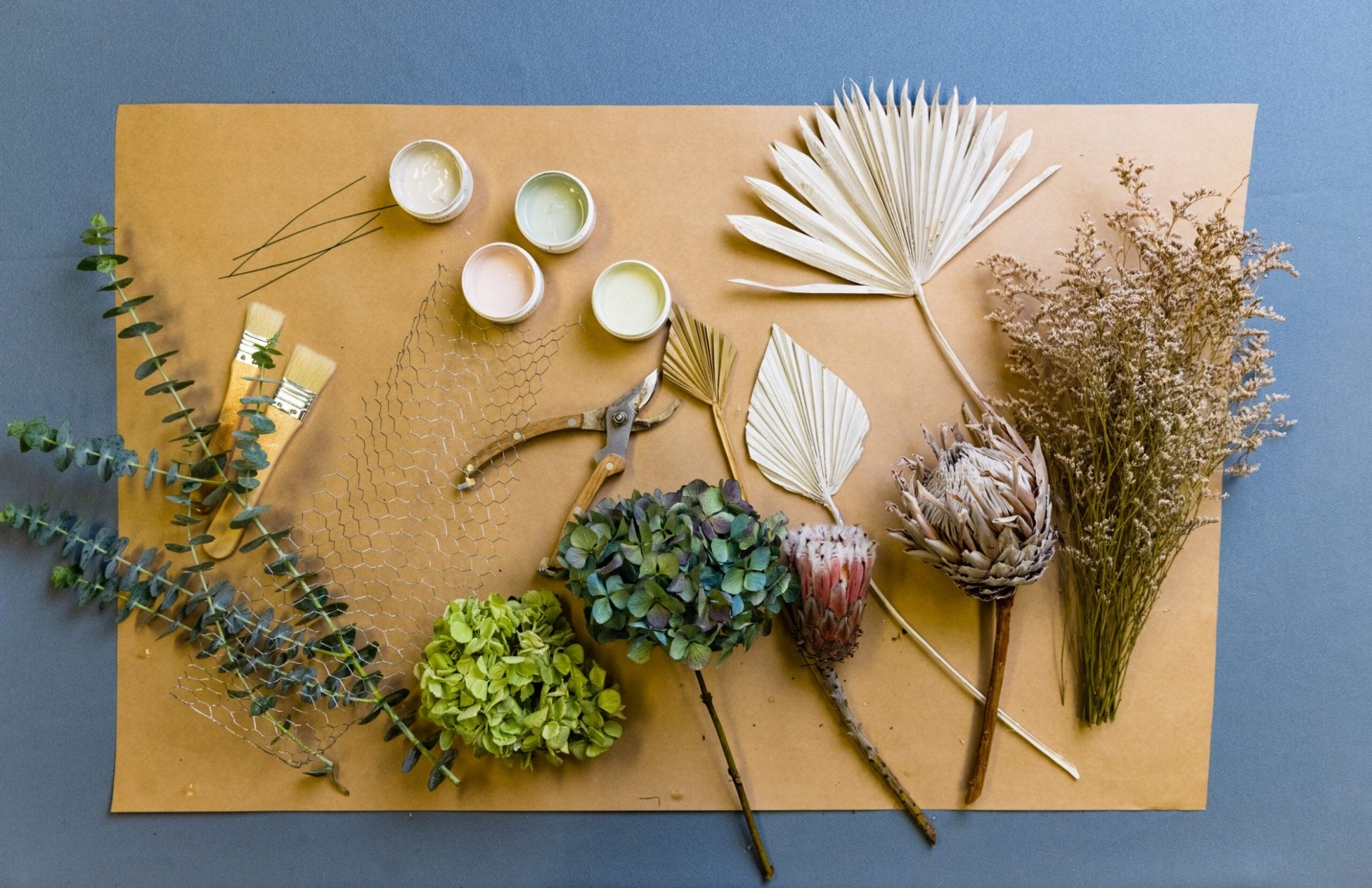 Brown wrapping paper with assortment of paint pots, greenery and paint brushes on top