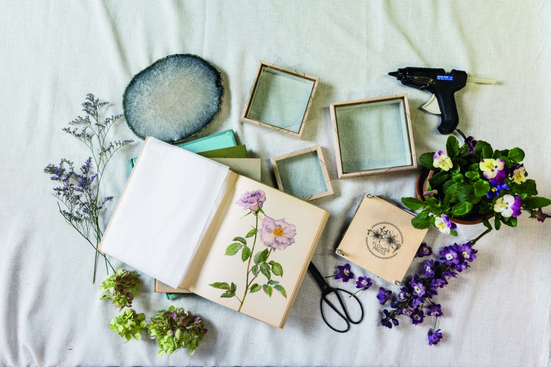 Pansies, limonium, hydrangea and delphinium flowers laid out on a white table along with other craft materials