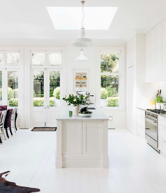 bright, white kitchen, with a skylight above the island and painted wooden floorboards