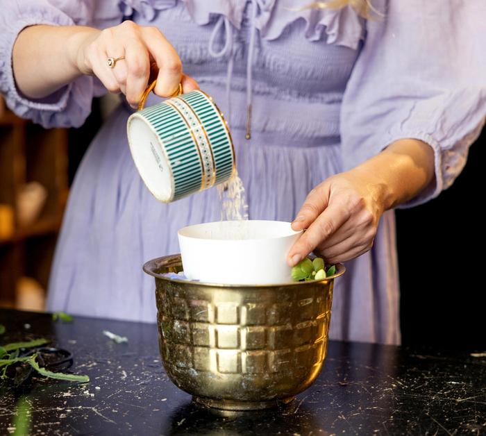 A woman in a purple dress pouring rice into a small vessel inside the medium bowl