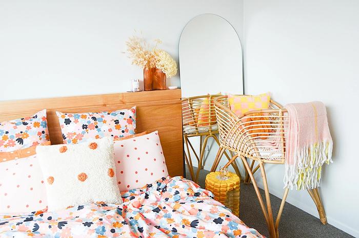 A bedroom with a bed, mirror, and bassinet.