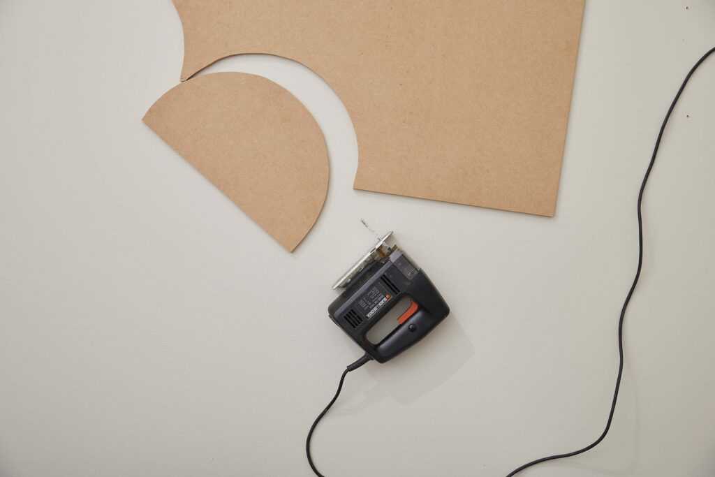 A piece of MDF board with an oval cut out and a jigsaw next to it