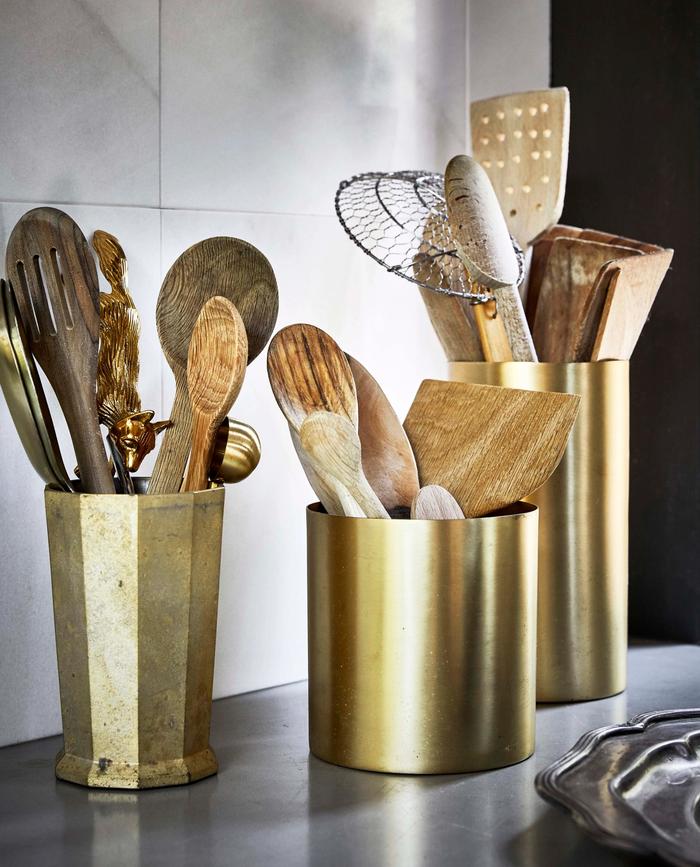 brass utensil holders with utensils in them on a grey bench