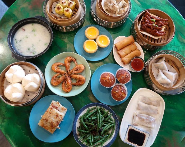 A selection of food on a table including steamed buns, spring rolls, green beans and dumplings.