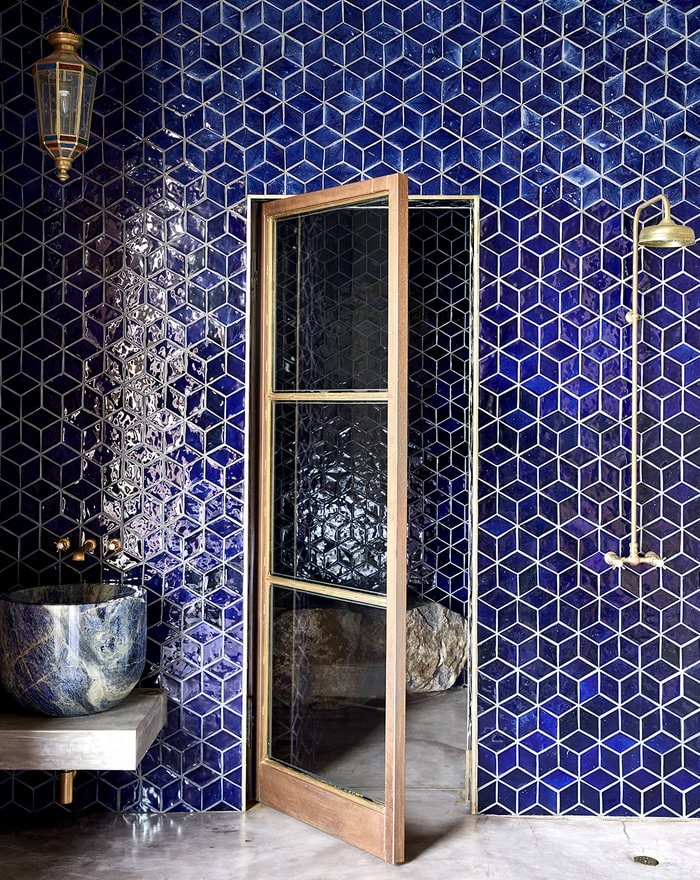 Dark blue tiled bathroom with gold shower head and hanging gold lamp