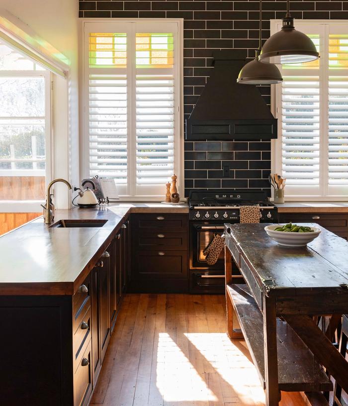 A black kitchen with shaker style cabinets, black subway tiles and a vintage island