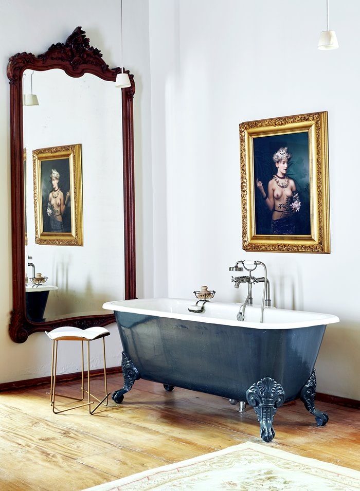 Boroque styled bathroom with wooden floors, vintage tub and classic portrait painting