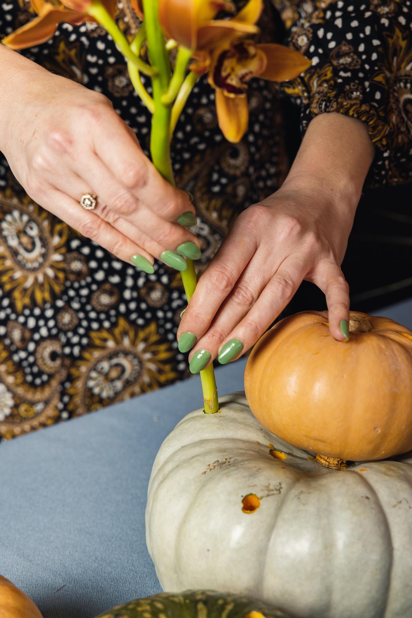 A yellow flower with a long stem being placed in a drill hole in a pumpkin