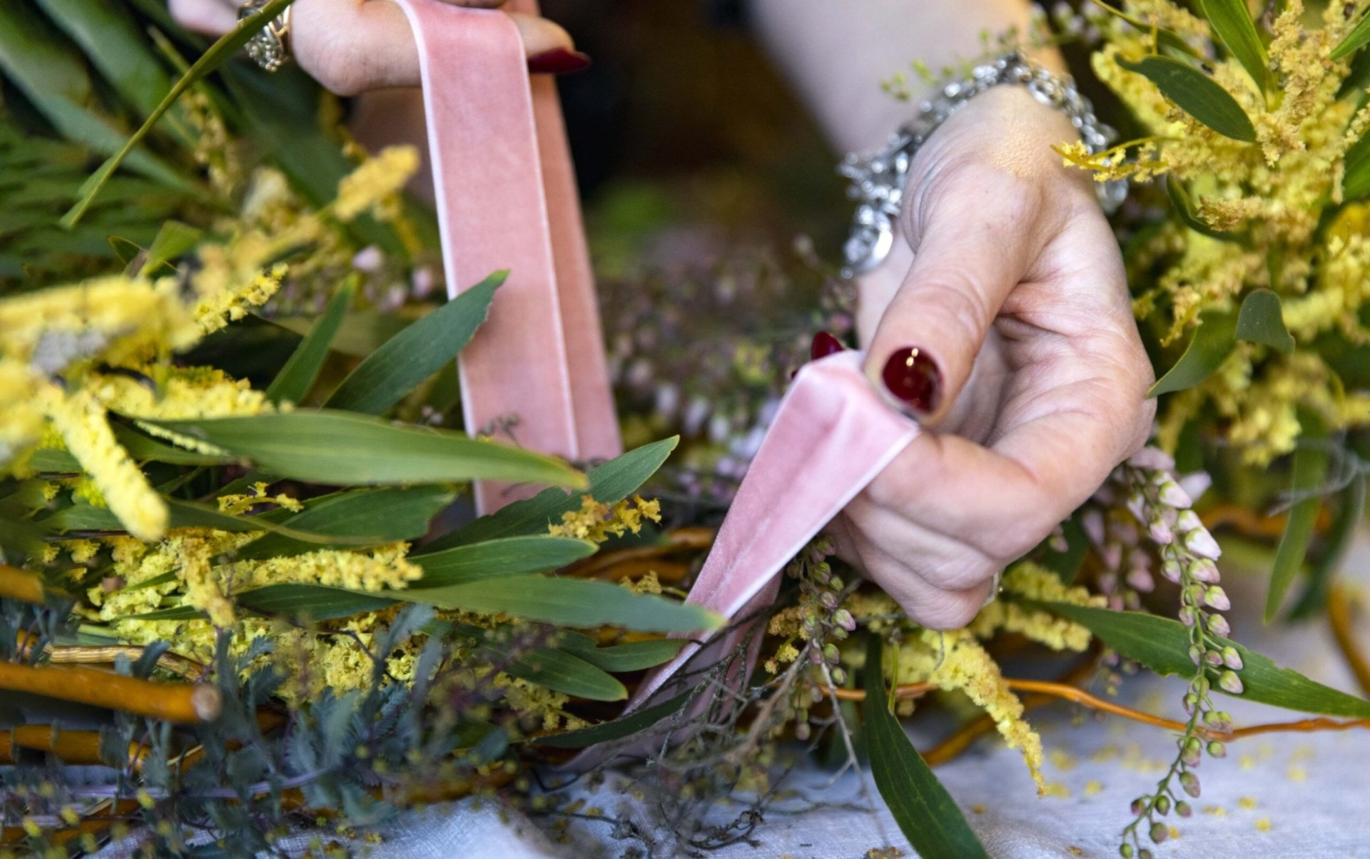 A pink ribbon being tied around a floral wreath